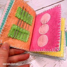 a hand is holding an open book with sewing pins in the cover and two different colors