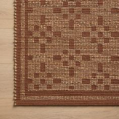 a brown area rug with squares and dots on the bottom, in front of a wooden floor