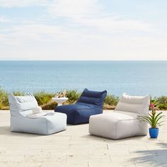 an outdoor seating area overlooking the ocean with blue and white cushions on it, along with potted plants