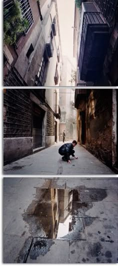 a person kneeling down on the ground in an alleyway with buildings and water puddles