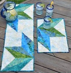 two quilted placemats sitting on top of a wooden table next to drinks