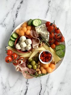 a white plate topped with lots of different types of cheese and meats next to cucumbers