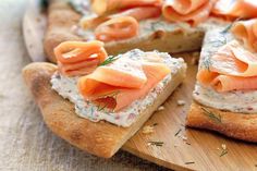 a wooden cutting board topped with slices of bread covered in cream cheese and smoked salmon