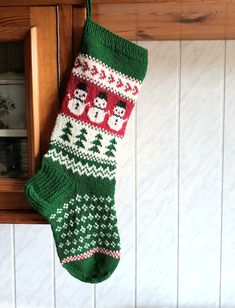 a green christmas stocking hanging from the side of a wooden door with snowmen on it