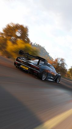 a black sports car driving down a road with trees in the background