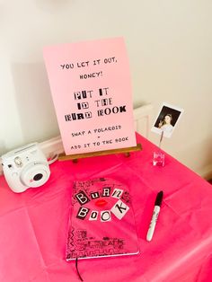 a pink table topped with a sign and other items next to a white polaroid camera