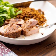 a white plate topped with meat and rice next to a green leafy salad on top of a wooden table