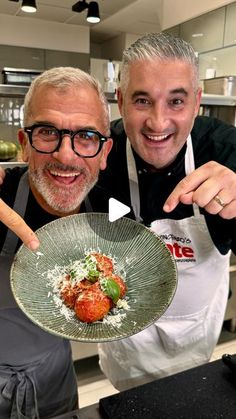 two men in aprons posing for the camera with a plate of food on it