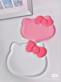 two pink hello kitty plates sitting next to each other on a white tablecloth with a framed photo in the background