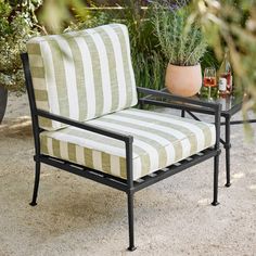 a striped chair with a glass of wine sitting on it's side table in front of a potted plant