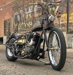 a custom motorcycle parked in front of a brick building with graffiti on the wall behind it