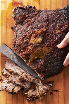 a person slicing meat on top of a wooden cutting board with a knife in it