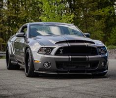 the front end of a silver mustang parked in a parking lot with trees behind it