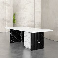 a black and white marble table with a plant in the corner on concrete flooring