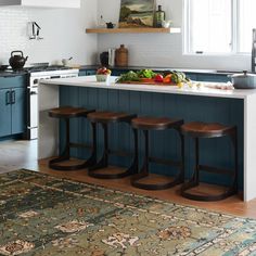 a kitchen with three stools in front of the island and an area rug on the floor