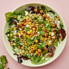 a salad with corn, lettuce and feta cheese in a white bowl