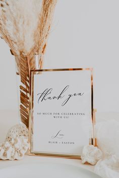 a thank you card sitting on top of a table next to a vase with feathers