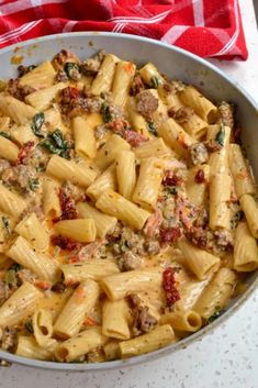 a pan filled with pasta and meat on top of a white countertop next to a red checkered towel