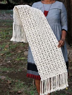 a woman standing next to a tree holding a white crocheted shawl