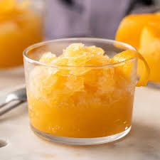 a small glass bowl filled with oranges on top of a counter next to two spoons