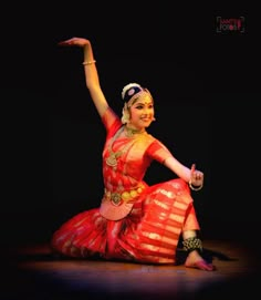 a woman in a red and yellow dress is dancing on stage with her arms outstretched