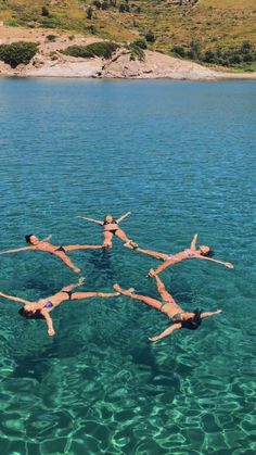 four people floating in the water with their arms around each other while doing acrobatic tricks