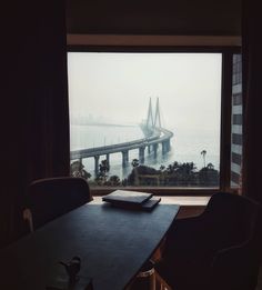 a table with a book on it in front of a window overlooking the ocean and bridge