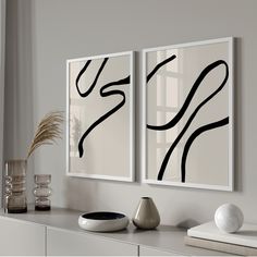 two black and white paintings hanging on the wall next to a vase with a plant in it