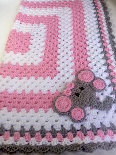 a crocheted baby blanket with a teddy bear on the front and pink, gray, and white border