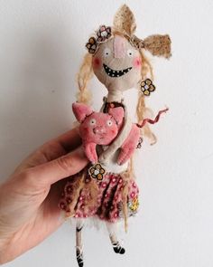 a hand holding a small doll in the shape of a pig with long blonde hair