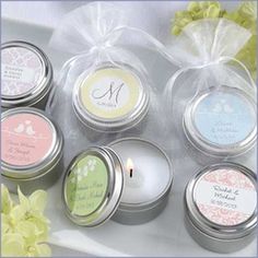 six personalized candles in tins on a table with flowers and ribbon around them