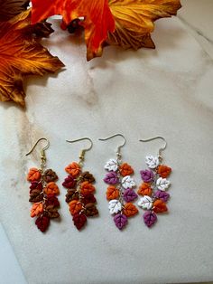 three pairs of earrings sitting on top of a white counter next to leaves and flowers