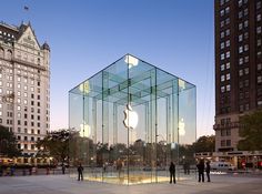 an apple store in the middle of a city with people standing around it at dusk