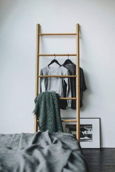 clothes are hanging on a wooden rack next to a bed