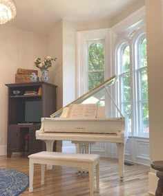 a white piano sitting in the corner of a living room next to a large window