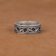 a silver ring sitting on top of a wooden table next to a brown surface with an intricate design