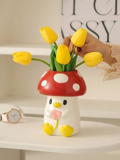 a mushroom vase with yellow tulips in it sitting on a table next to a watch