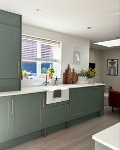 a large kitchen with green cabinets and white counter tops is pictured in this image, there are flowers on the window sill