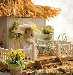 there is a small toy mouse on the beach next to flowers and a table with chairs