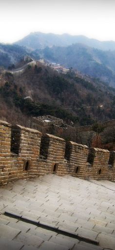 a man riding a skateboard on the side of a stone wall with mountains in the background