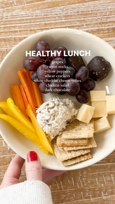 a person holding a plate with cheese, crackers and fruit on it that says healthy lunch