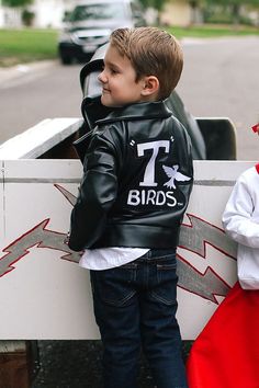 two little boys dressed up as superheros and one is wearing a leather jacket with the number seven birds on it