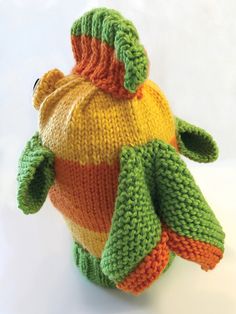 a knitted stuffed animal with an orange, yellow and green hat on it's back