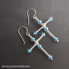 two cross earrings with blue beads hanging from the end of each ear wire, on a black surface