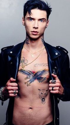 a shirtless man with tattoos on his chest and jacket over his shoulder, posing for the camera