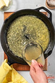 a person is pouring some liquid into a skillet with food on the table next to it