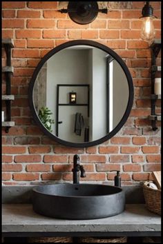 Round mirror on a brick wall above a black sink, with rustic shelves and lighting. Industrial Farmhouse Bathroom Ideas