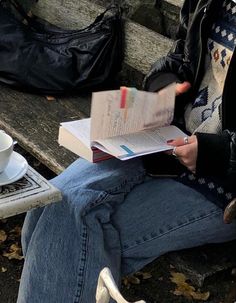 a woman sitting on a bench reading a book and holding a coffee cup in her hand