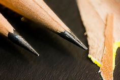 two pencils sitting next to each other on top of a black surface with yellow tips