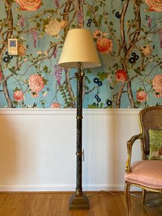 a lamp sitting on top of a wooden floor next to a wall covered in flowers